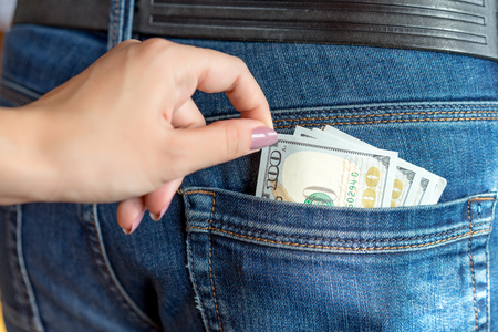 Female hand of a young woman stealing 100 dollar money bill out of pocket man jeans.の写真素材