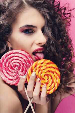 Curly beautiful girl with yellow and red lollipop on pink backgroundの写真素材