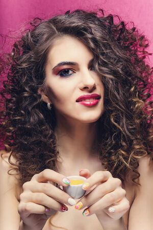 beautiful curly girl with colourful manicure smile and drink from a small cupの写真素材
