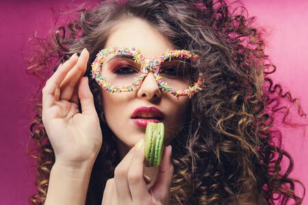 Beautiful girl eat green macaroon in confectionery dressing glassesの写真素材