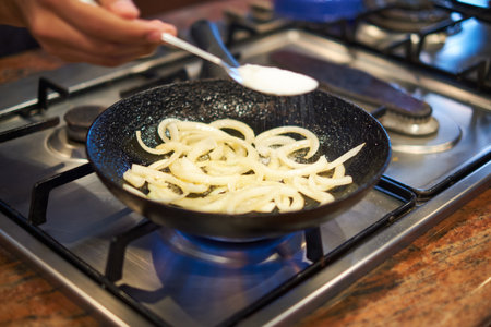 cooking onions on a frying pan on a gas stove in the kitchenの写真素材