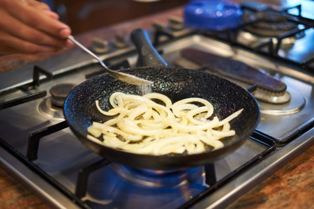 Cooking onions on a gas stove in a restaurant kitchen, close upの写真素材
