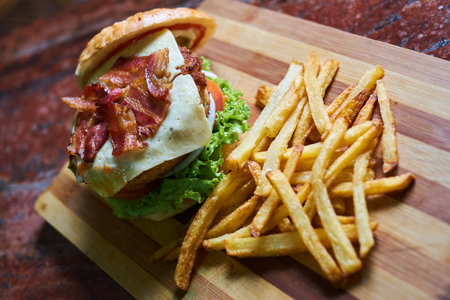 Burger with bacon and french fries on a wooden cutting board.の写真素材