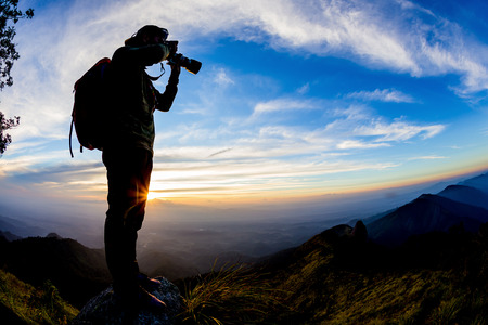 Silhouette of Young man with backpack taking a photo on the top of mountains