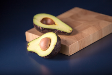 Halved avocado on a rustic table. Fresh avocado on black background. Vegetarian or healthy eating.