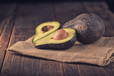 Halved avocado on a rustic table. Fresh avocado on black background. Vegetarian or healthy eating.の写真素材