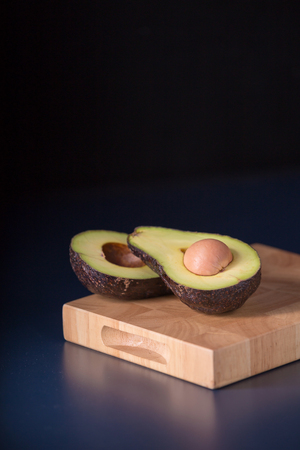 Halved avocado on a rustic table. Fresh avocado on black background. Vegetarian or healthy eating.
