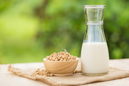 Soy milk and soy beans in wooden cup with abstract blurred forest nature backgroundの写真素材