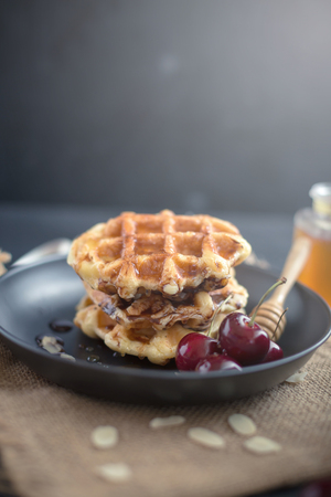 Honey on waffles with cherry berries on dark wooden background. breakfast concept.の写真素材