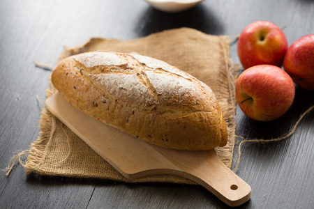 French bread baguette cut on wooden board with knife.  with red apple.