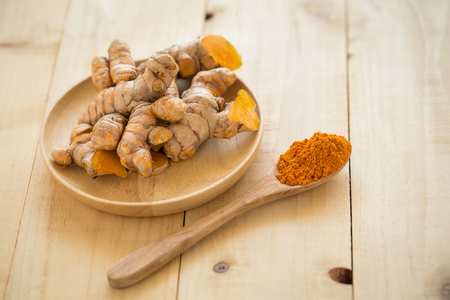 Turmeric powder in a wooden spoon and fresh turmeric on wooden background.の写真素材