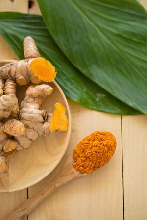 Turmeric powder in a wooden spoon and fresh turmeric on wooden background.の写真素材