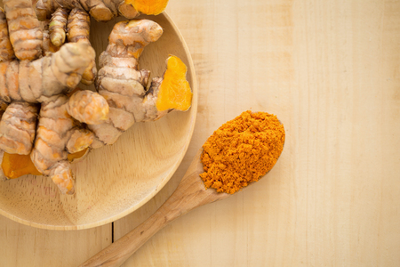 Turmeric powder in a wooden spoon and fresh turmeric on wooden background.の写真素材