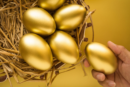 Financial success. Man holding a golden egg. Golden Egg on golden background.の写真素材