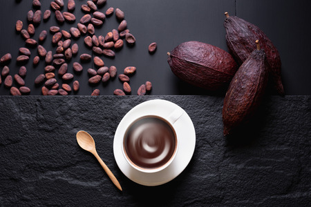 Hot chocolate and Cocoa pod cut exposing cocoa seeds on dark table, top view with copy space.の写真素材
