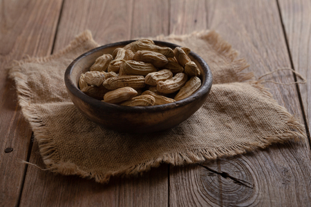 Peanuts in nutshell in a piece of wooden bowl on sackcloth.