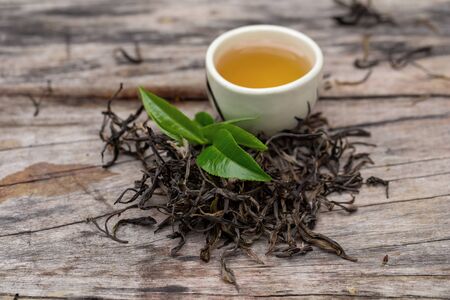 Glass of tea on a wooden table and fresh green tea leaves.