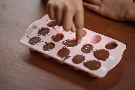 Children's hands squeeze using pastry bag filling hot melt chocolate into silicone mold.  Selective...