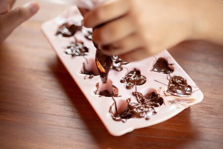Children's hands squeeze using pastry bag filling hot melt chocolate into silicone mold.  Selective...