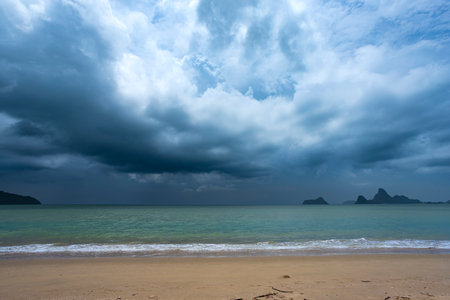 Fluffy clouds drift across a bright summer sky above a tropical beach with turquoise waves lapping at the shoreの写真素材