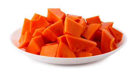 Ripe Holland papaya with smooth orange skin and vibrant flesh. Cut into pieces on a white ceramic plate, isolated on a white backgroundの写真素材