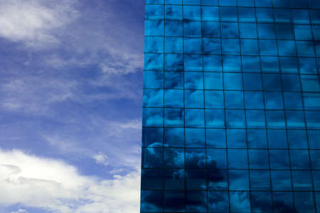 A modern blue glass building reflecting a clouded skyの写真素材