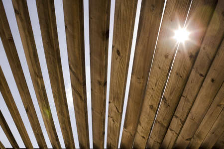 A wooden roof with sun flare and sky in the background.の写真素材
