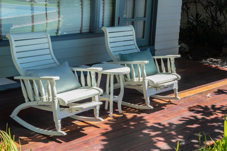 Cozy white rocking chairs on a sunny wooden porch.の写真素材