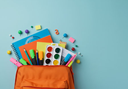 School supplies in orange backpack on blue background. Back to school conceptの素材