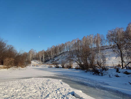 Huge wide snow-covered river. The branches of dry trees hang over the frozen river. Beautiful winter...