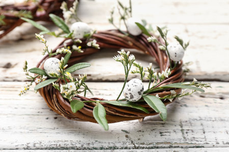 Stylish Easter wreath with leaves, flowers and eggs on light wooden background