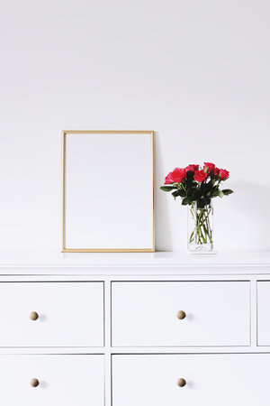 Golden horizontal frame and bouquet of rose flowers on white furniture, luxury home decor and design...