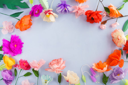 Colorful handmade paper flowers on light blue background with copyspace in the centerの写真素材