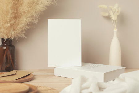 Blank paper card, greeting card mock up. decoration with dried Bunny Tail and pampas grass, Front view, Beautiful Bunny Tail grass in vase and white book on wood table and beige cement wall backgroundの写真素材