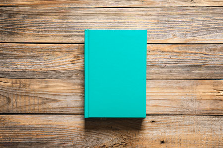 Closed green book on wooden background, top view, copy space.