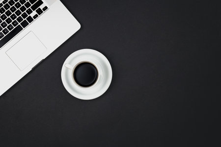 Laptop and cup of black coffee on black background, top view, minimalist workplace.