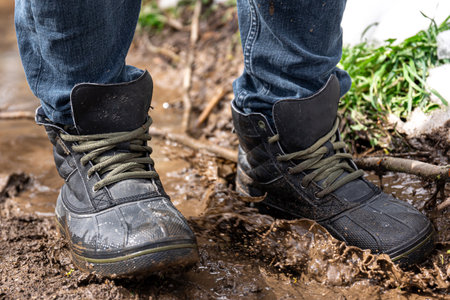 A man in jeans and boots walks through the swamp in rainy weather, in the countryside, legs close up.の写真素材