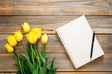 Blank notepad and yellow tulips on a wooden background, top view, copy space.の写真素材