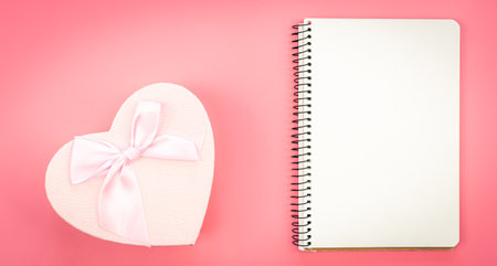 Blank notebook and heart shaped gift box on pink background, top view, copy space.の写真素材