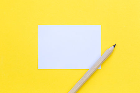 Wooden pencil and a piece of paper on a yellow background, flat lay, copy space.の写真素材