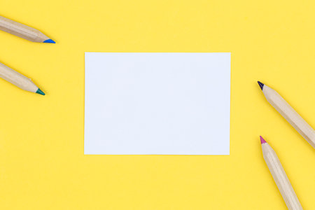 Multicolored wooden pencils and blank piece of paper on a yellow background, flat lay.の写真素材