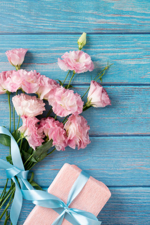 Beautiful eustoma flowers and gift box on blue wooden background