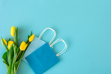 Flat lay blue background with yellow tulip flowers in paper bag, spring concept, copy space.の写真素材
