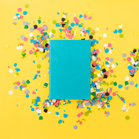 Blue book and confetti on yellow background. Flat lay, top viewの写真素材