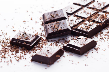 Dark chocolate bar and its broken pieces and some powder around over a white background