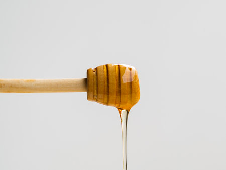 Honey dripping from a wooden honey dipper isolated on white background