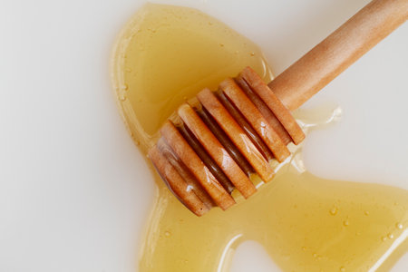 Honey dripping from a wooden honey dipper on a white backgroundの写真素材