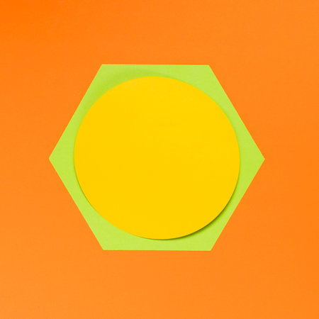 Yellow and green paper hexagon on orange background. Minimal concept.