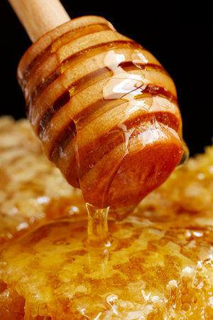 Honey dripping from a wooden honey dipper on a black backgroundの写真素材