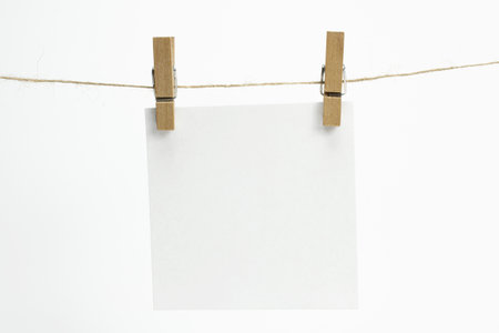 Single empty paper sheet for notes that hang on a rope with clothespins and isolated on white. Blank white cards on rope mockup template.の写真素材